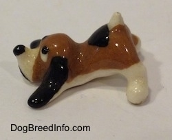 The left side of a figurine of a brown with white and black Hound Dawg figurine. The figurine has its front on the ground and its back side in the air.